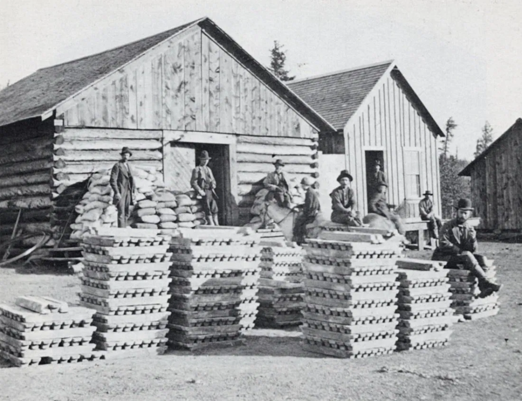 Workers pose with stacked ore ingots outside a Leadville, Colorado mining operation, circa the 1880s silver boom.