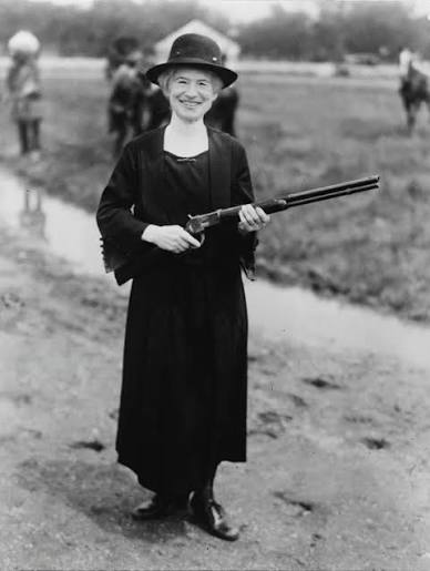 Annie Oakley smiles with her rifle in one of her later photographs, taken years after the little girl who had hunted squirrels to feed her siblings became one of the most famous women in the world.